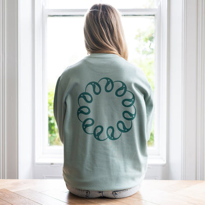 Girl sitting at window wearing Every Little Thread Sweatshirt in Aloe Colour. Back View of logo