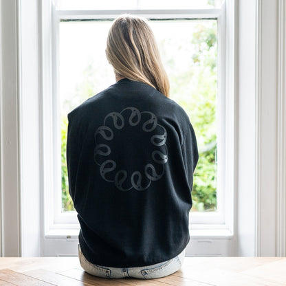 Girl sitting at window wearing Every Little Thread Sweatshirt in Black Colour. Back View of logo