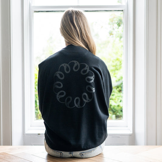 Girl sitting at window wearing Every Little Thread Sweatshirt in Black Colour. Back View of logo