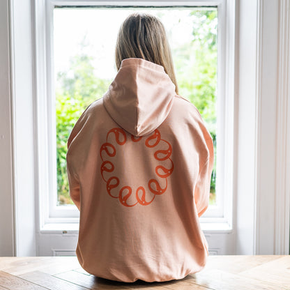 Girl sitting at window wearing Every Little Thread Hoodie in Peach Colour. Back View of logo