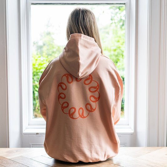 Girl sitting at window wearing Every Little Thread Hoodie in Peach Colour. Back View of logo