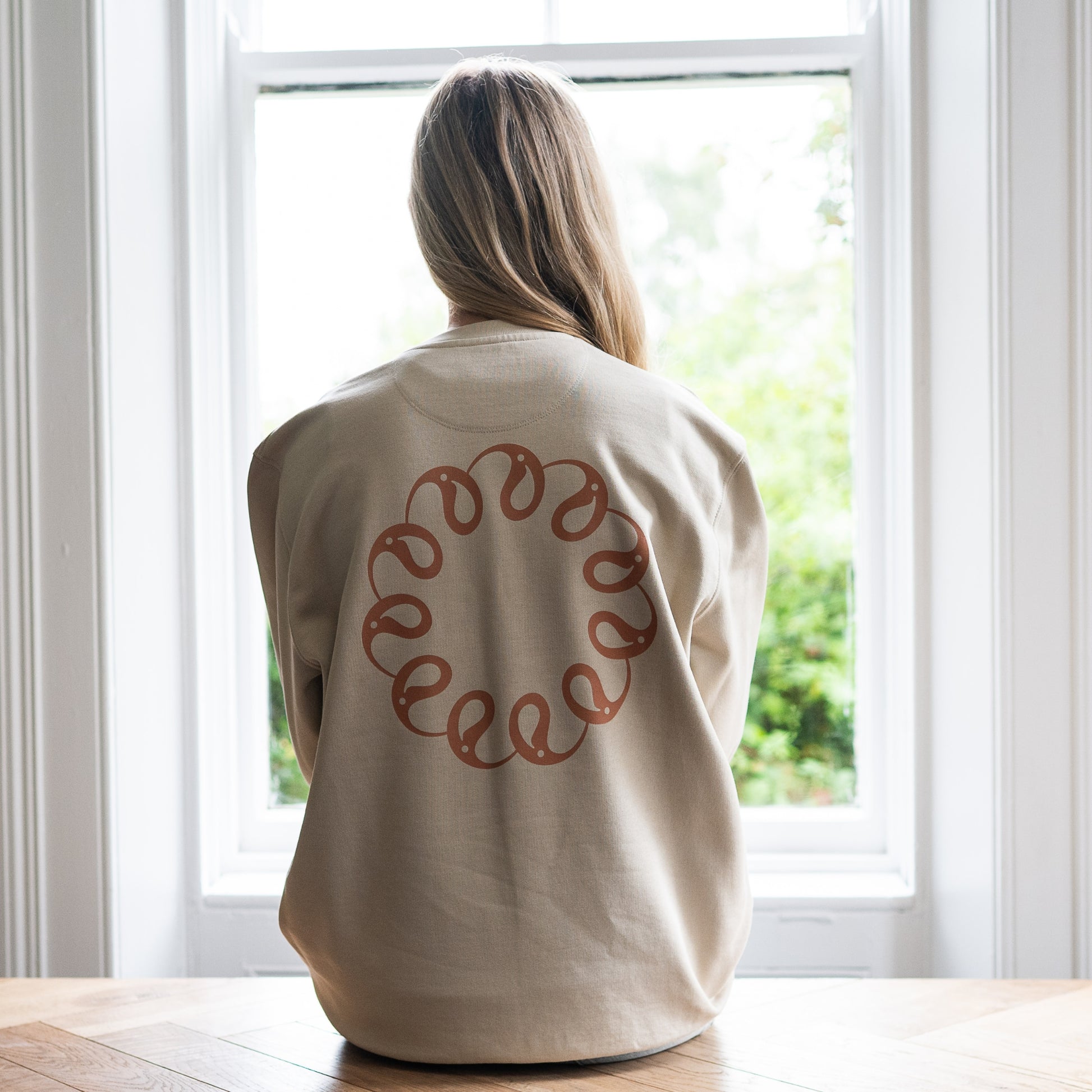 Girl sitting at window wearing Every Little Thread Sweatshirt in Sand Colour. Back View of logo
